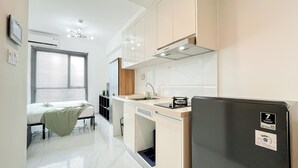 A modern kitchen with a built-in dishwasher, a refrigerator, and a window with blinds. - Homey Studio At Sky House Alam Sutera Apartment (Tangerang)