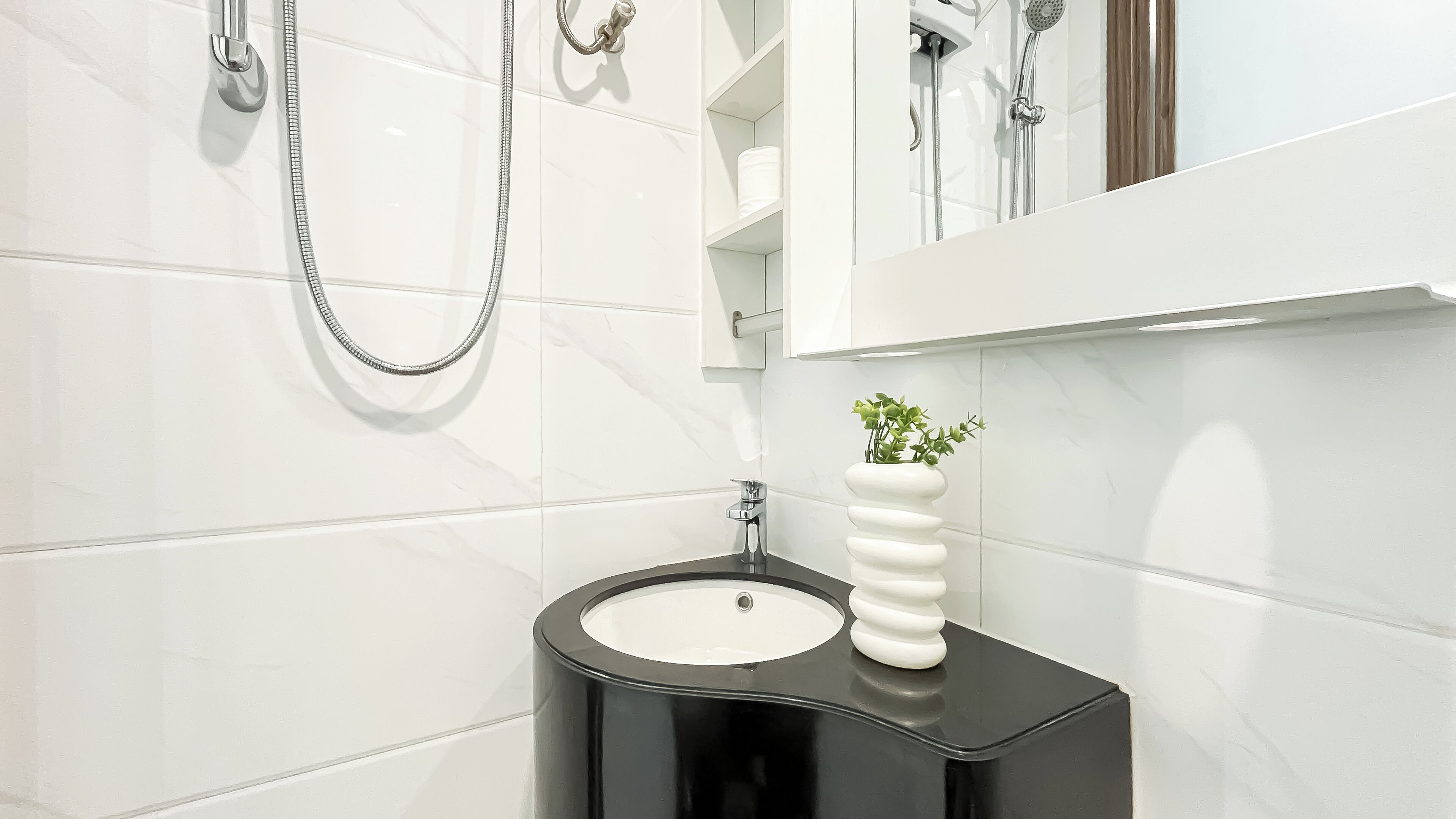 Une salle de bain avec des murs recouverts de carreaux blancs, un lavabo noir et un miroir au-dessus.