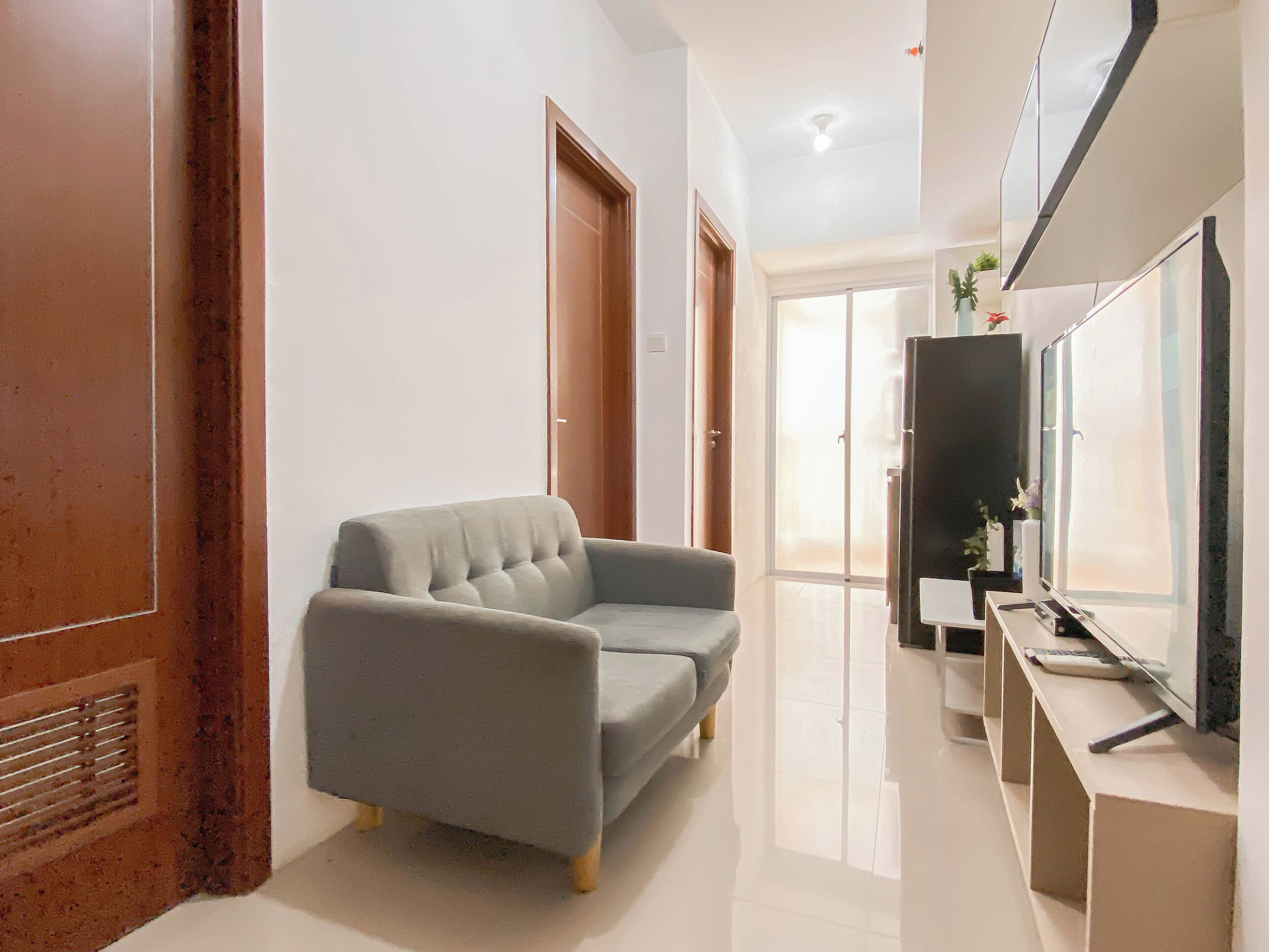 A modern hallway with a grey sofa, a flat-screen TV, and a mirror on the wall.