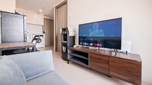 A modern living room with a grey sofa, a wooden entertainment unit with a flat-screen TV, a coffee machine, and a washing machine in the background. - Trendy 1Br Apartment At Anwa Residence (South Tangerang)