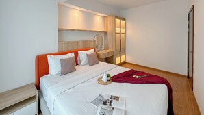 A modern hotel room with a neatly made bed, a bedside table, a small bedside table, and a large mirror. - Cozy And Homey 2Br At Grand Sungkono Lagoon Apartment (Surabaya)