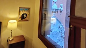 Una stanza con soffitto in legno, una finestra con cornice decorativa, un tavolino con lampada e un quadro appeso al muro.