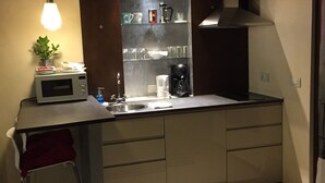 Una cucina compatta con forno a microonde, macchina del caffè ed scaffali con stoviglie.