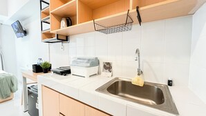 Eine moderne Küche mit weißen Fliesen, einer Edelstahl-Spüle, Holzschränken und einer eingebauten Ablage mit Wasserkocher und Korb.