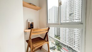 Ein Zimmer mit Holzstuhl, einem Regal mit einem Buch und einem Fenster mit Blick auf hohe Gebäude.