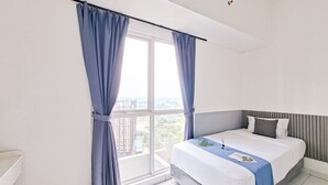 Ein Hotelzimmer mit großem Fenster, einem Bett mit blauer Bettdecke und Blick auf die Stadtlandschaft.