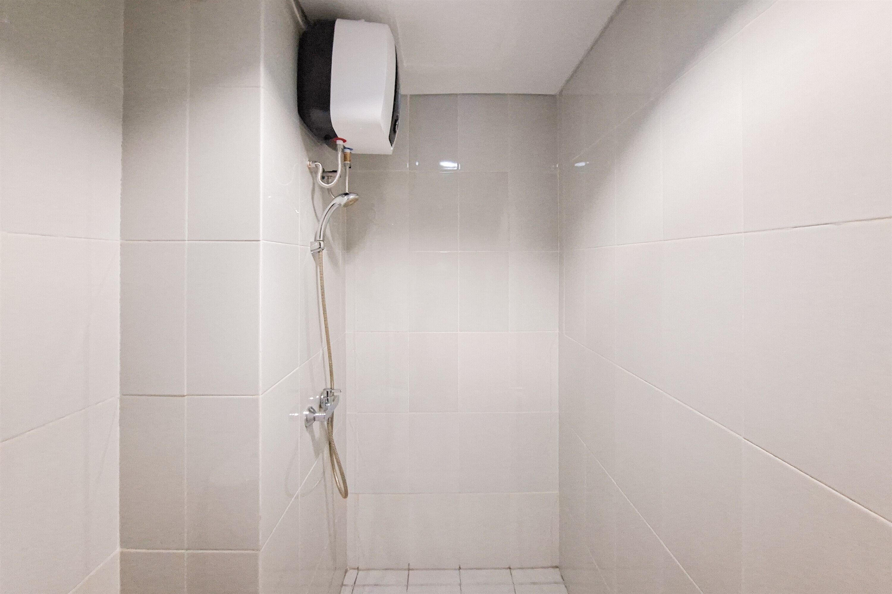 Un pequeño box de ducha con azulejos, un cabezal de ducha de mano y un dispensador de jabón en la pared.