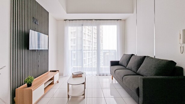 Ein modernes Wohnzimmer mit einem grauen Sofa, einer Holzbank, einem kleinen weißen Tisch und einem an einer gestreiften Wand befestigten Fernseher.