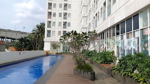 A modern building with a swimming pool, surrounded by greenery and a clear sky. - Basic Studio Near Cisauk Station At Serpong Garden Apartment (Cisauk)
