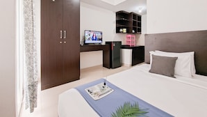 A modern hotel room with a large bed, a desk with a computer, a wardrobe, and a television. - Basic Studio Near Cisauk Station At Serpong Garden Apartment (Cisauk)