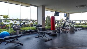 Un gimnasio con equipo de ejercicio, un saco de boxeo y amplias ventanas con vistas a un jardín.