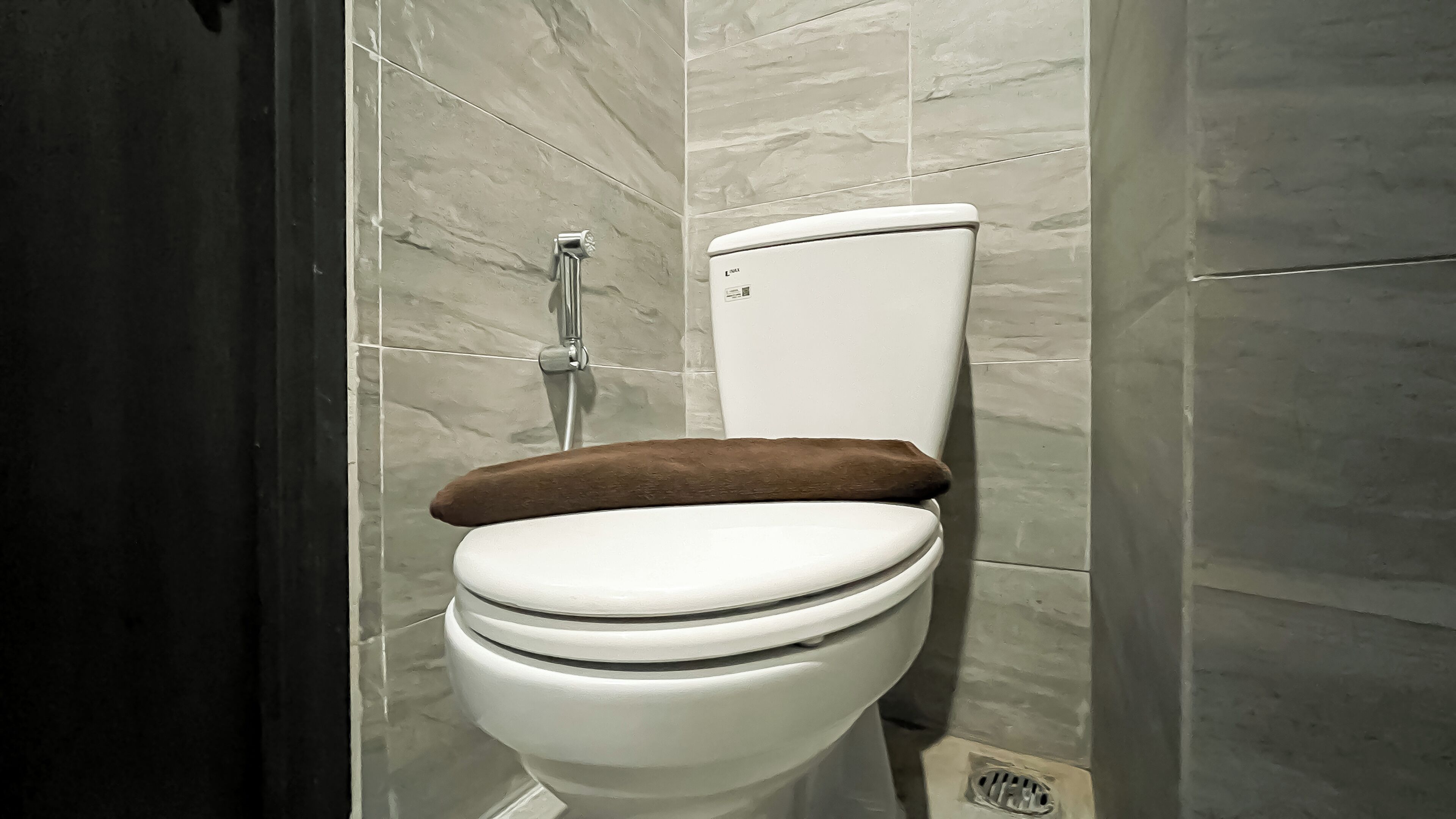 A white toilet with a brown seat and a wall-mounted flush handle.