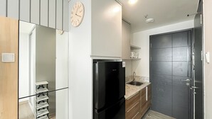 A compact kitchen with a black refrigerator, a wooden cabinet, and a clock on the wall. - Restful And Modern Studio At Collins Boulevard Apartment (Tangerang)
