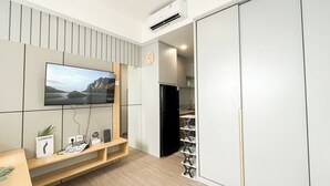 A modern kitchen with a built-in TV, a black refrigerator, and a wooden shelf with books and a plant. - Restful And Modern Studio At Collins Boulevard Apartment (Tangerang)