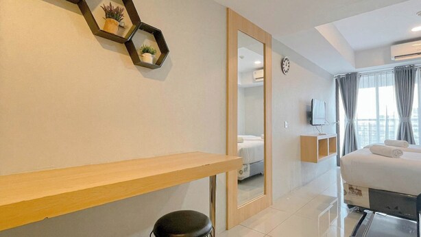 Ein modernes Hotelzimmer mit einem Holztisch, einem schwarzen Stuhl, einem Bett mit weißen Bettwäsche, einem Fernseher und einem großen Fenster mit Vorhängen.