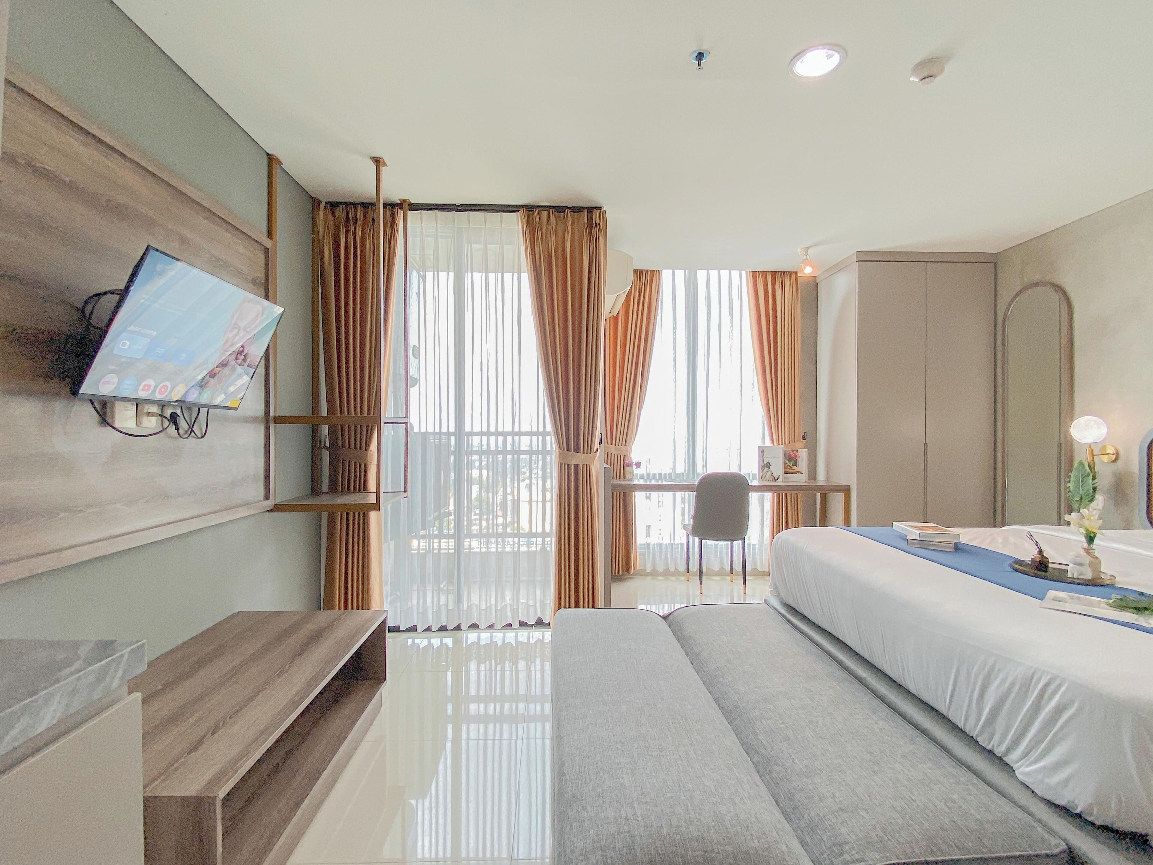 A modern hotel room with a bed, bedside table, TV mounted on the wall, and a desk with a chair.