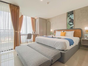 Habitación de hotel con cama, escritorio, silla y una ventana grande con cortinas.