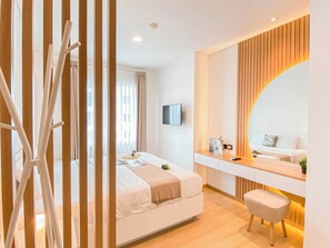 Una habitación de hotel moderna con una cama, un escritorio con computadora, un televisor y un espejo grande.