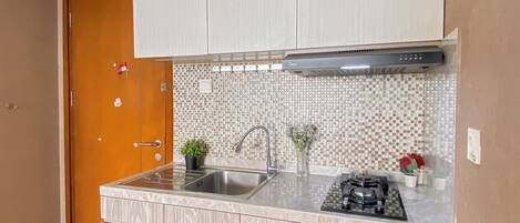 A compact kitchen with a wooden door, white cabinets, a tiled backsplash, a stainless steel sink, and a gas stove.