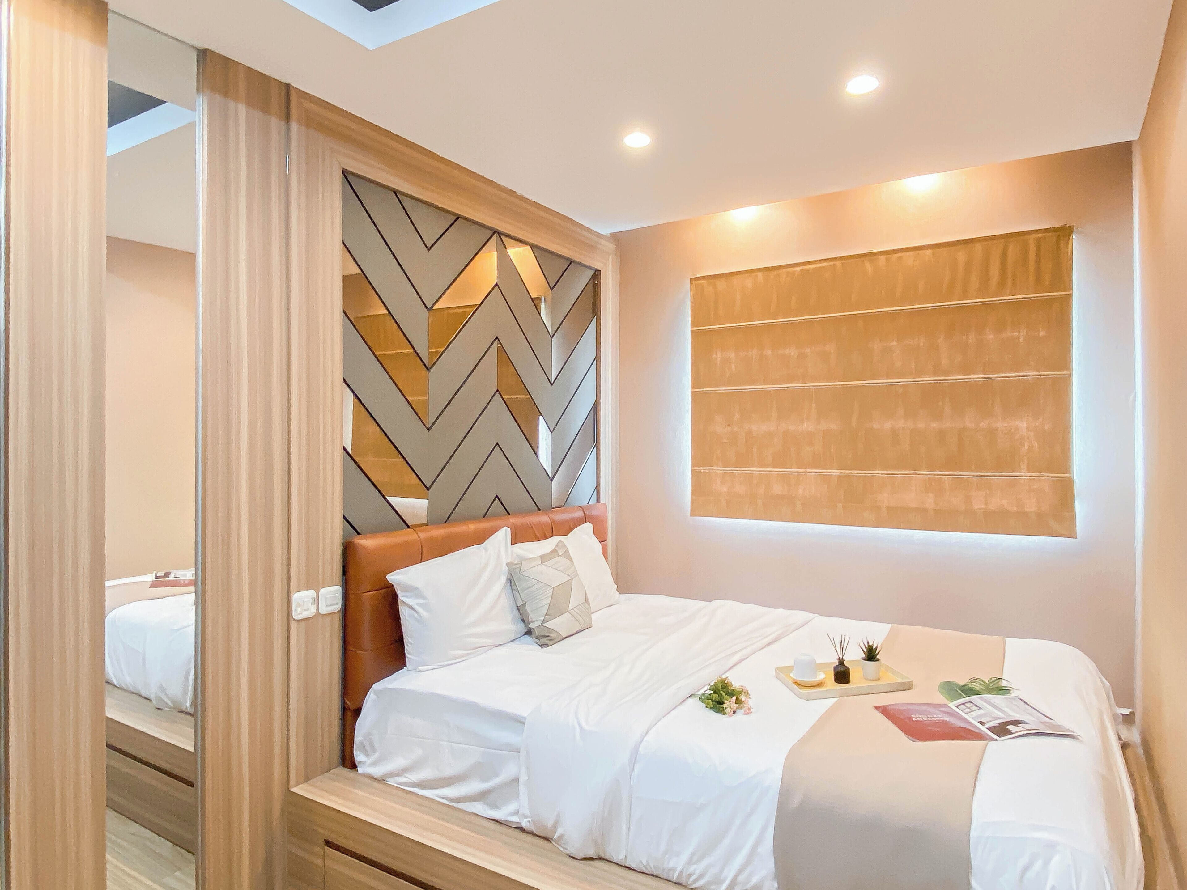 Un dormitorio moderno con una cabecera de tablero encalado, un ventanal con persianas, una mesita de noche con una planta y una cama bien hecha.