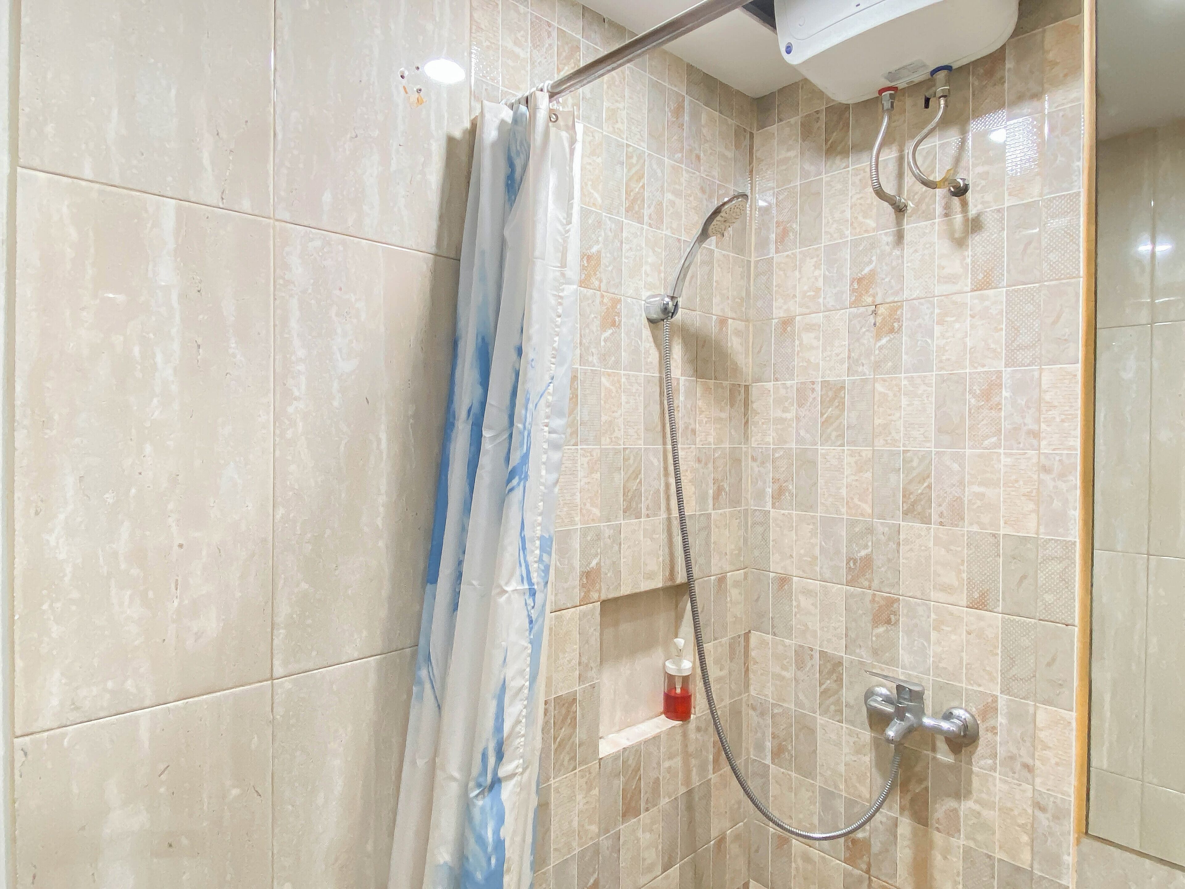 Un área de ducha con cortina, cabezal de ducha de mano y grifo empotrado en la pared.