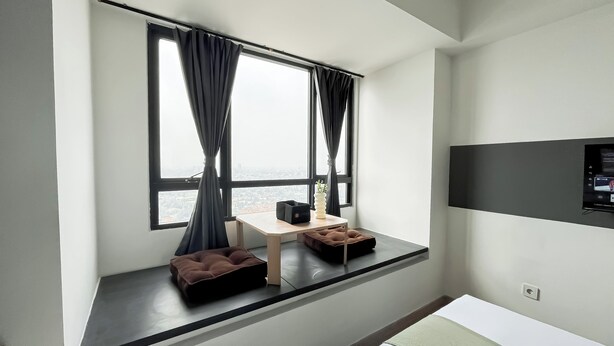 Una habitación de hotel moderna con un ventanal grande, un escritorio pequeño, un banco acolchado y un televisor montado.