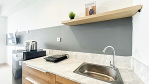 Una cocina moderna con un lavamanos integrado, una tetera, una cafetera y una estantería con una planta y una caja.