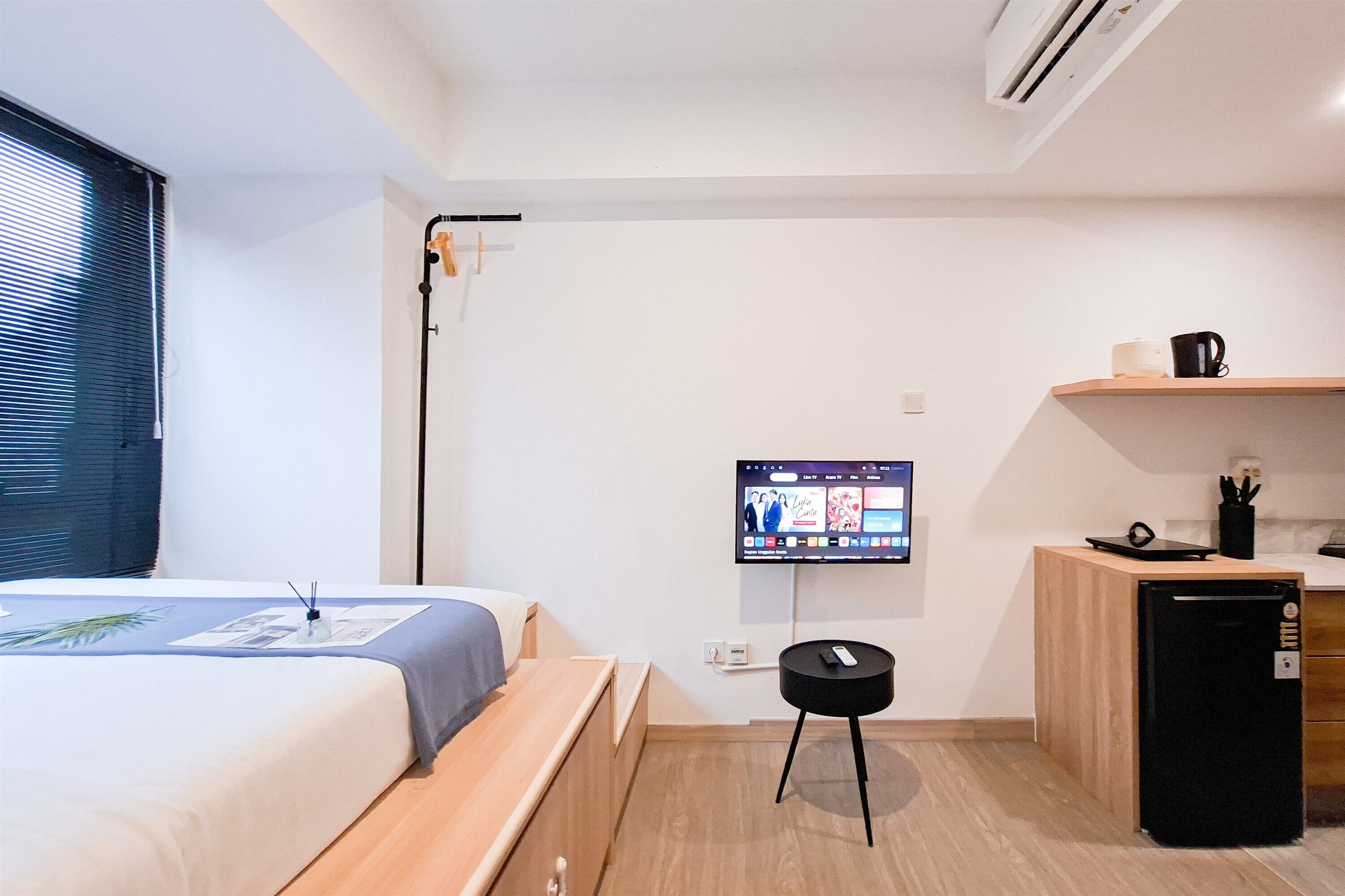 Una habitación de hotel pequeña con cama, kitchenette, televisión y escritorio.