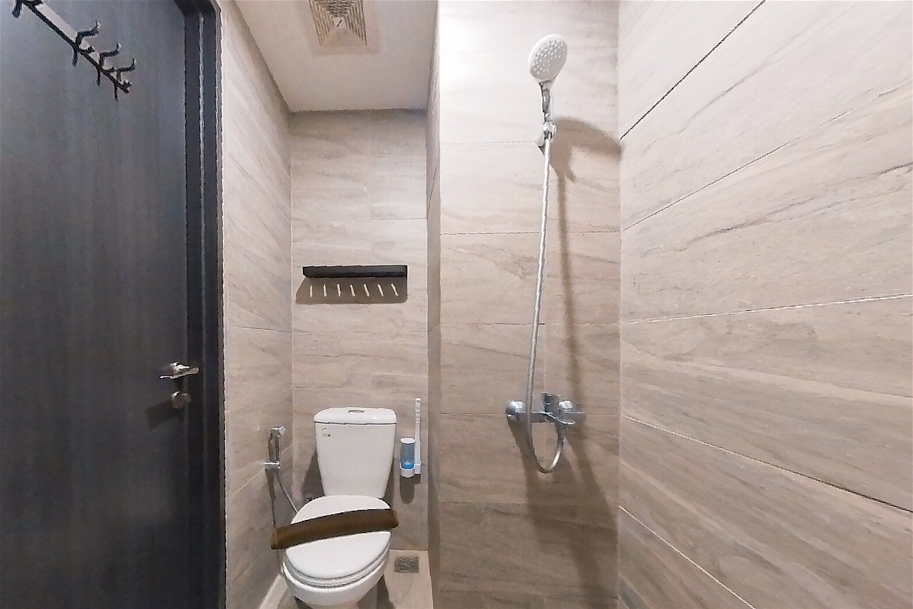 Un baño pequeño con azulejos, un inodoro, un cabezal de ducha y un perchero para toallas.