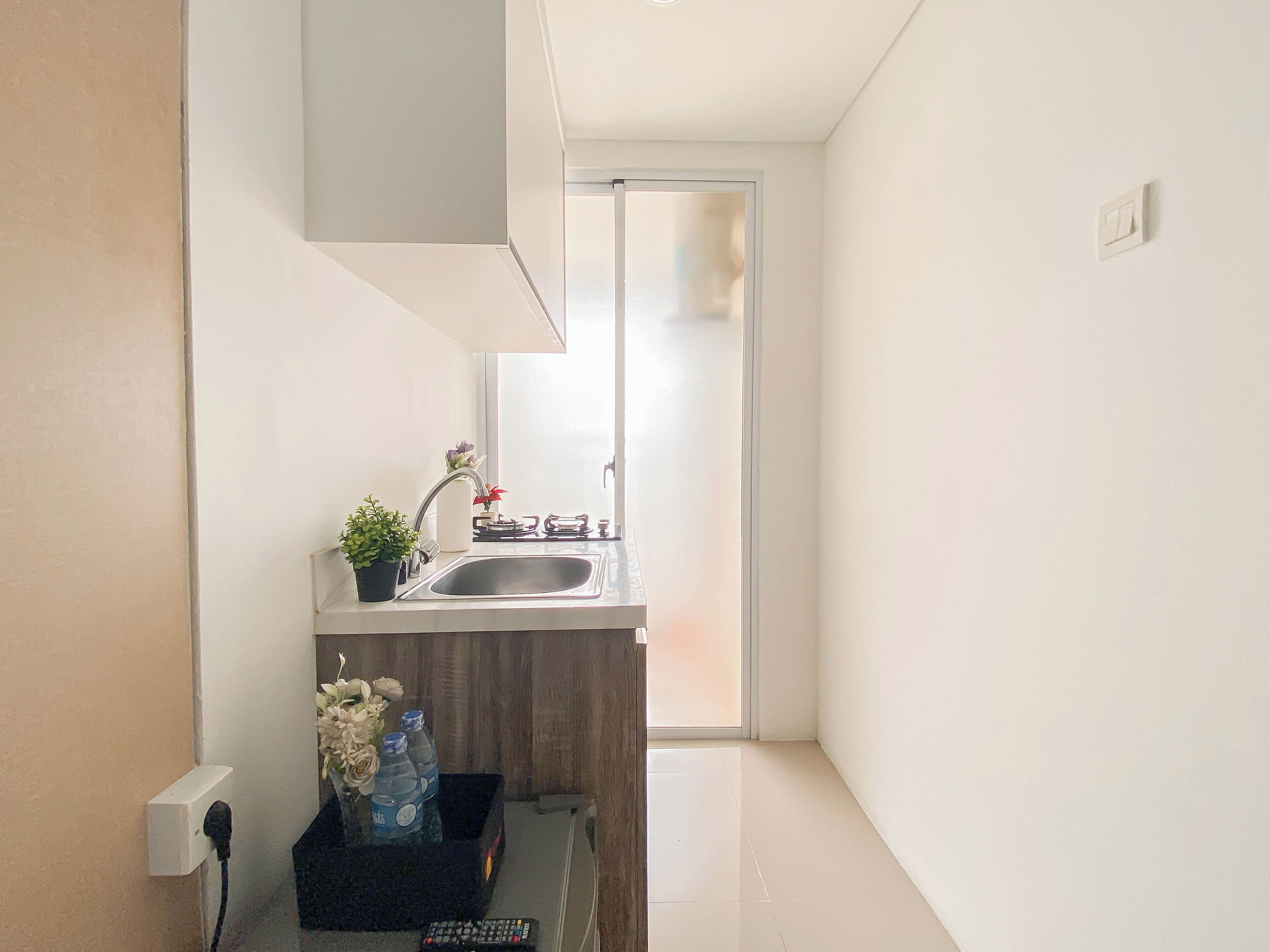 A small kitchen with a sink, a potted plant, and a vase of flowers. There is a window with a view of the outside.