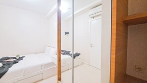 A hotel room with a bed, a wardrobe, and a mirror. - Standard 2Br At Parahyangan Residence Apartment (Bandung)
