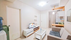 A modern living room with a flat-screen TV, a coffee table, a sofa, and a kitchen area with a sink and cabinets. - Standard 2Br At Parahyangan Residence Apartment (Bandung)