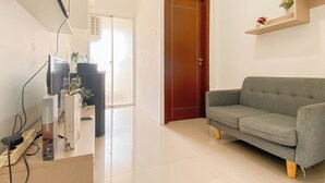 A living room with a grey sofa, a wooden door, and a white tiled floor. - Ivory Nest 1Br At Vittoria Residence Apartment (Jakarta)