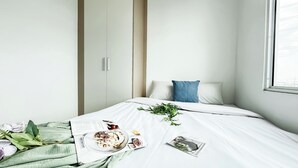 Una cama bien hecha con ropa blanca, una almohada azul y una planta verde al lado.