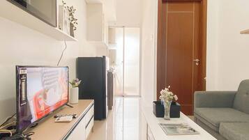 A modern living room with a flat-screen TV, a refrigerator, a coffee table with a magazine, a grey sofa, and a door leading to another room.