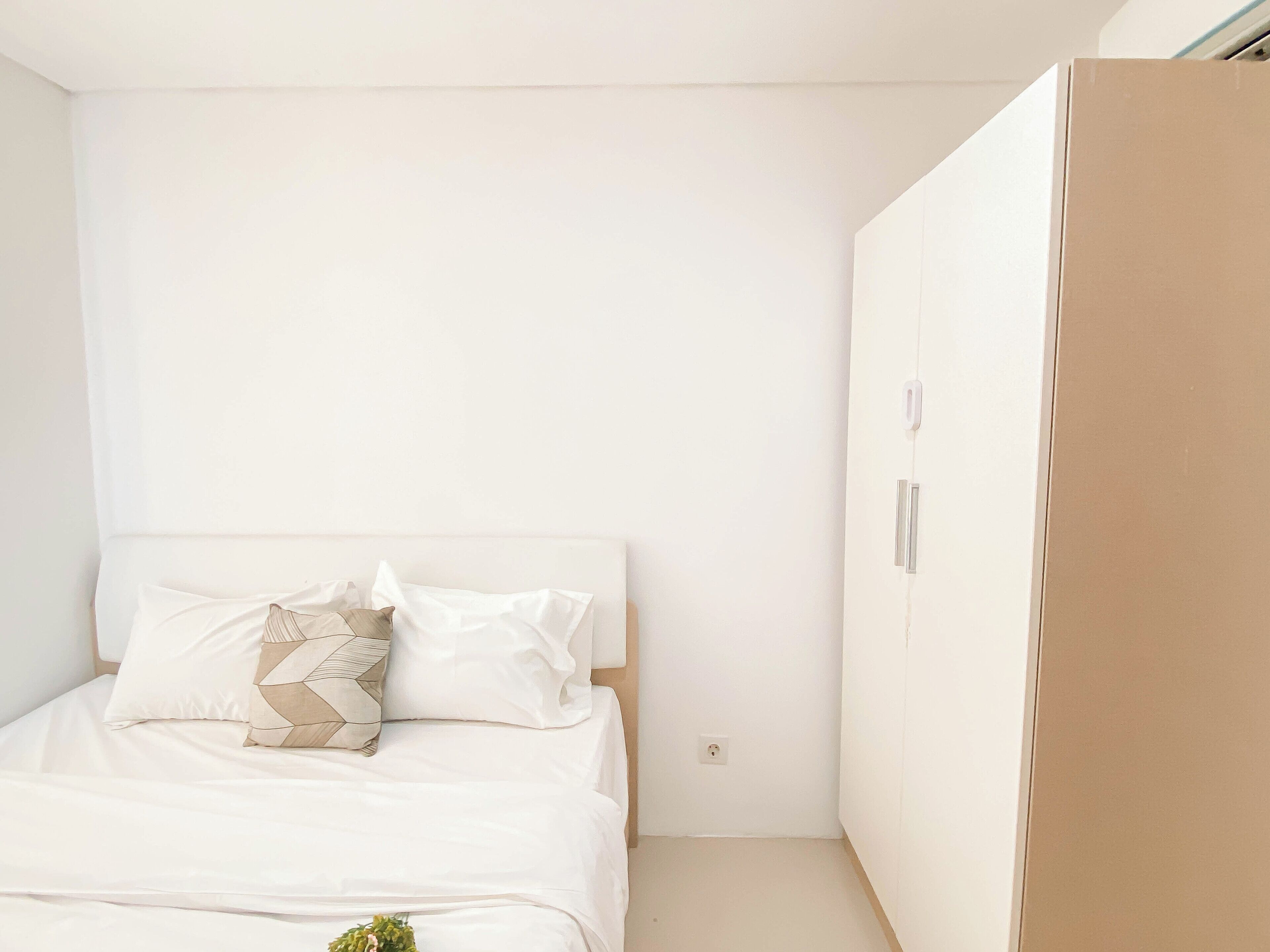A minimalist bedroom with a bed, a wardrobe, and a power outlet on the wall.
