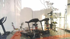 Un gimnasio con equipo de ejercicio, incluyendo cintas de correr y máquinas de pesas, en una sala con ventanales amplios.