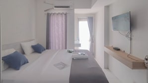 Una habitación de hotel con cama, televisor montado en la pared y ventana con cortinas.