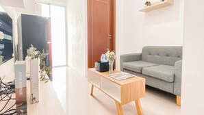 Una sala moderna con un sofá gris, una mesa de centro de madera y un televisor sobre un mueble bajo. Hay una puerta con una pequeña planta en la pared superior.