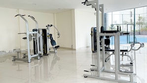 Ein sauberer, moderner Fitnessraum mit verschiedenen Trainingsgeräten, großen Fenstern und einem Fliesenboden.