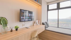 Ein moderner Büroraum mit großem Flachbildfernseher an der Wand, einem Holztisch, einem bequemen Stuhl, einer kleinen Pflanze und Blick auf die Stadt durch ein großes Fenster.