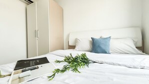 A hotel room with a bed, white bedding, a blue pillow, a white headboard, and a wardrobe. - Minimalist Look 1Br At Apartment Vittoria Residence (Jakarta)