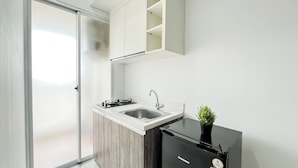 A modern kitchen with a built-in island, stainless steel sink, and a compact black refrigerator. - Minimalist Look 1Br At Apartment Vittoria Residence (Jakarta)