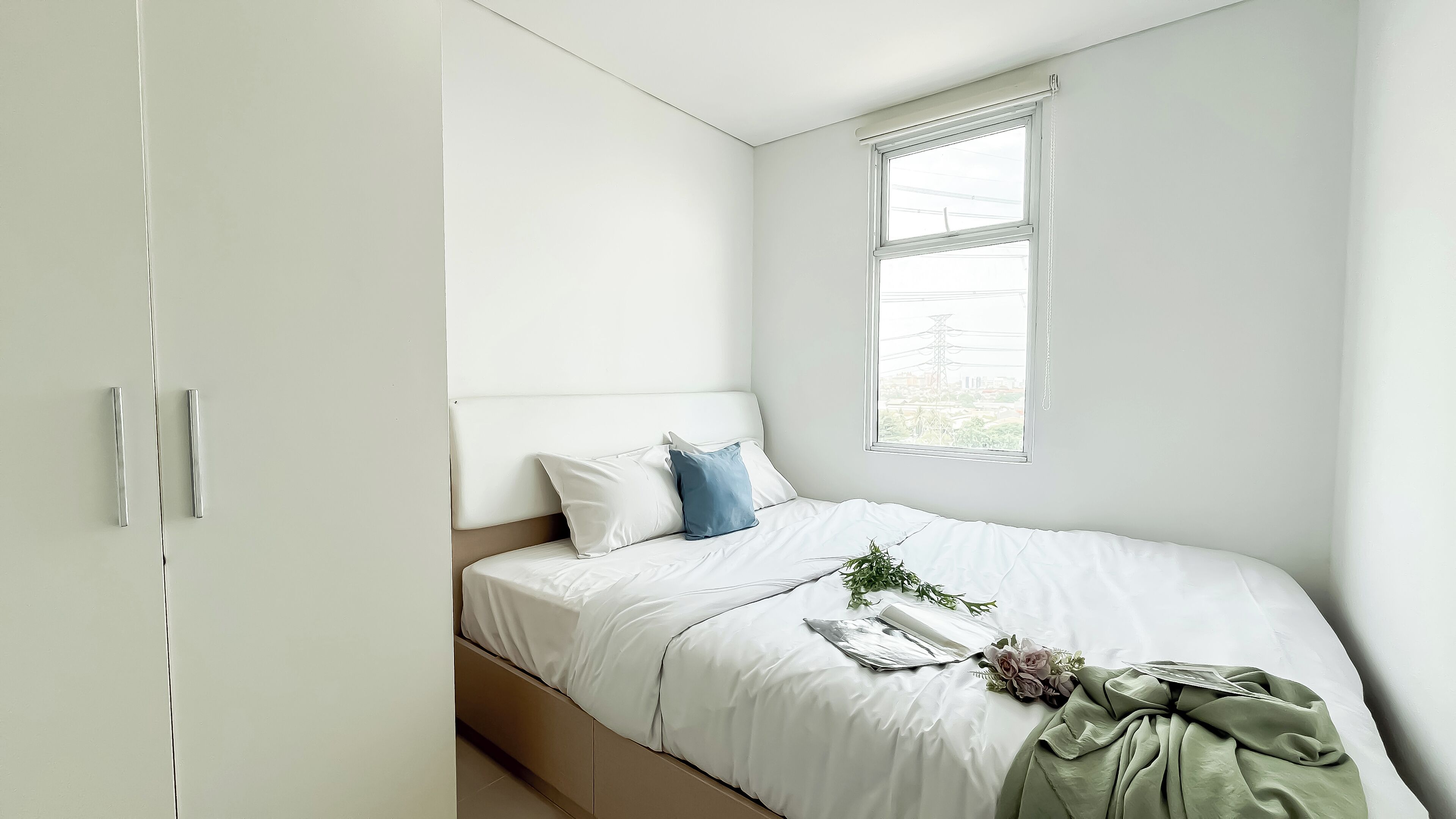 A bedroom with a bed, white walls, a window, and a wardrobe.