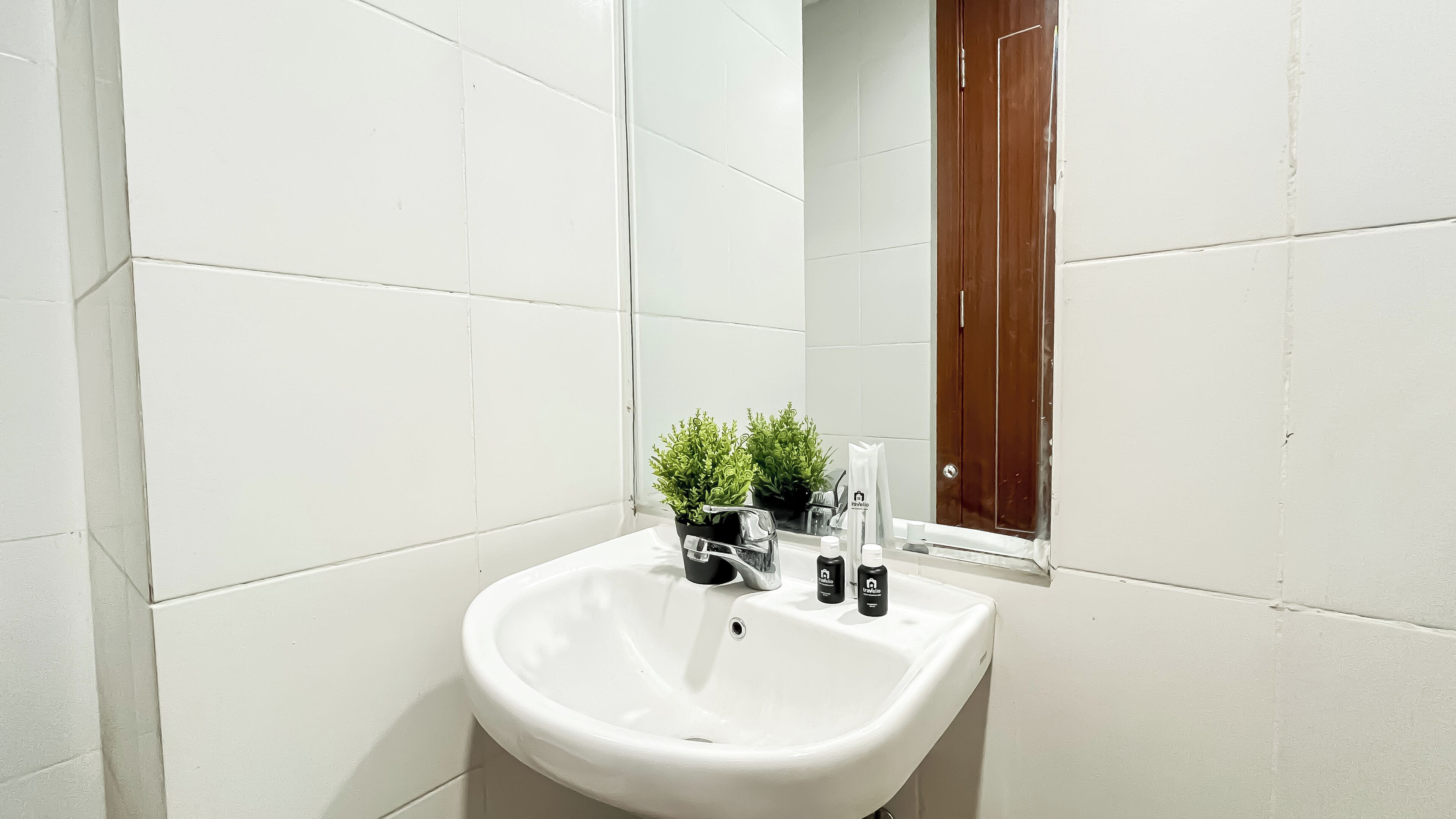 A bathroom with white tiles, a sink, a mirror, and a small potted plant.