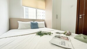 A neatly made bed with white bedding, a blue pillow, and a magazine on the bed. - Restful 2Br At Vittoria Residence Apartment (Jakarta)