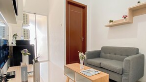 A modern living room with a grey sofa, a wooden coffee table, and a door. There are small plants on a shelf above the sofa. - Convenient 1Br Apartment At Vittoria Residence (Jakarta)