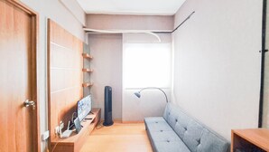 A compact room with a wooden wardrobe, a grey sofa, a small table, and a TV on a wooden stand. - Well Furnished 2Br At Apartment Suites @Metro (Bandung)