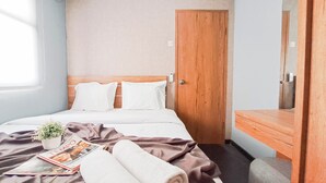 A hotel room with a bed, a wooden door, a mirror, a bedside table, a window, and a plant. - Well Furnished 2Br At Apartment Suites @Metro (Bandung)