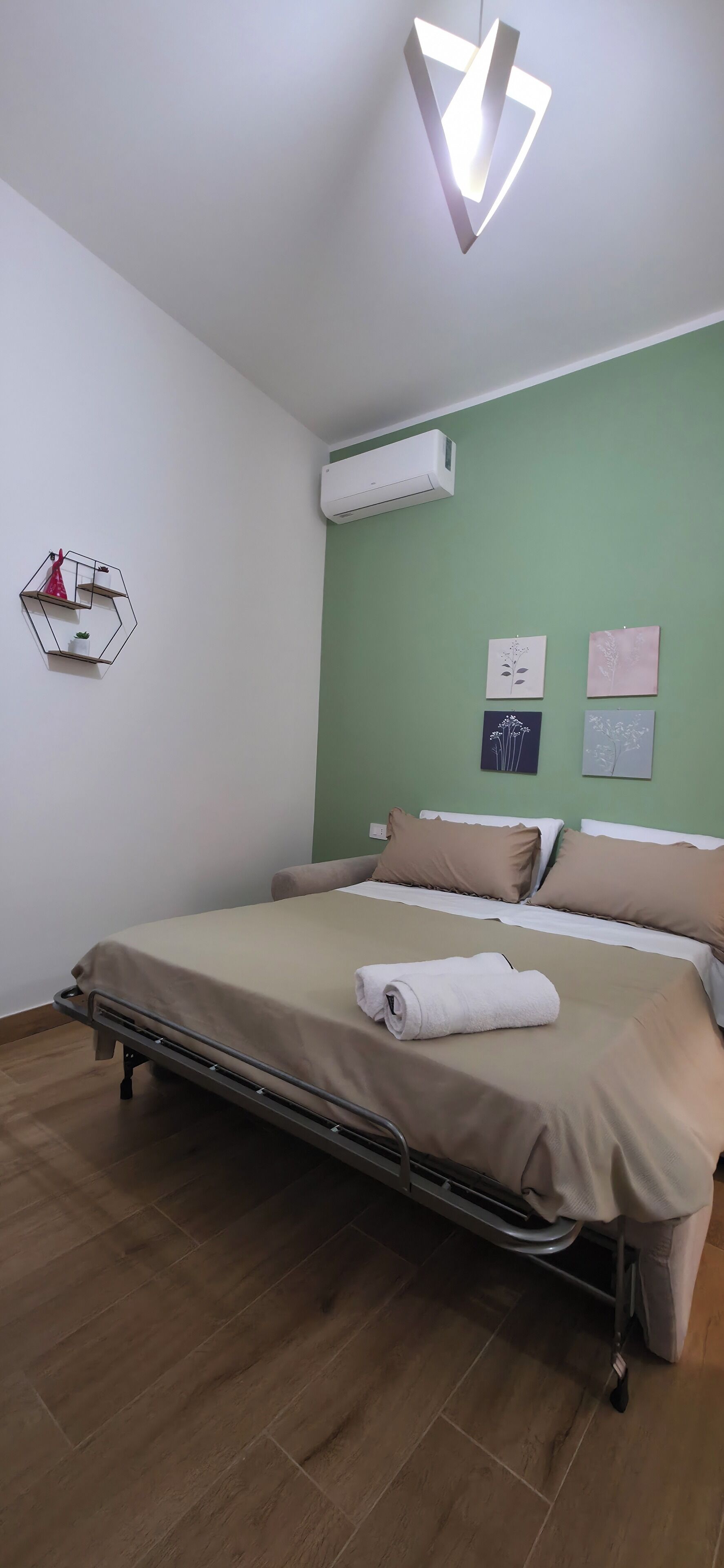 A neatly arranged bedroom with a bed, a bedside table, a wall-mounted air conditioner, and a geometric light fixture.
